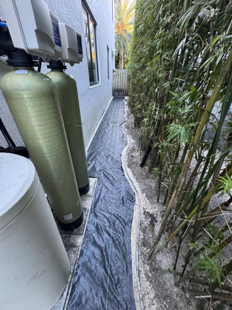 Dark installation underlay in a narrow passage between a white wall and bamboo.