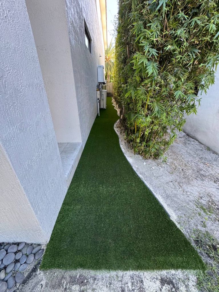 Turf in a narrow passage between a white wall and bamboo.