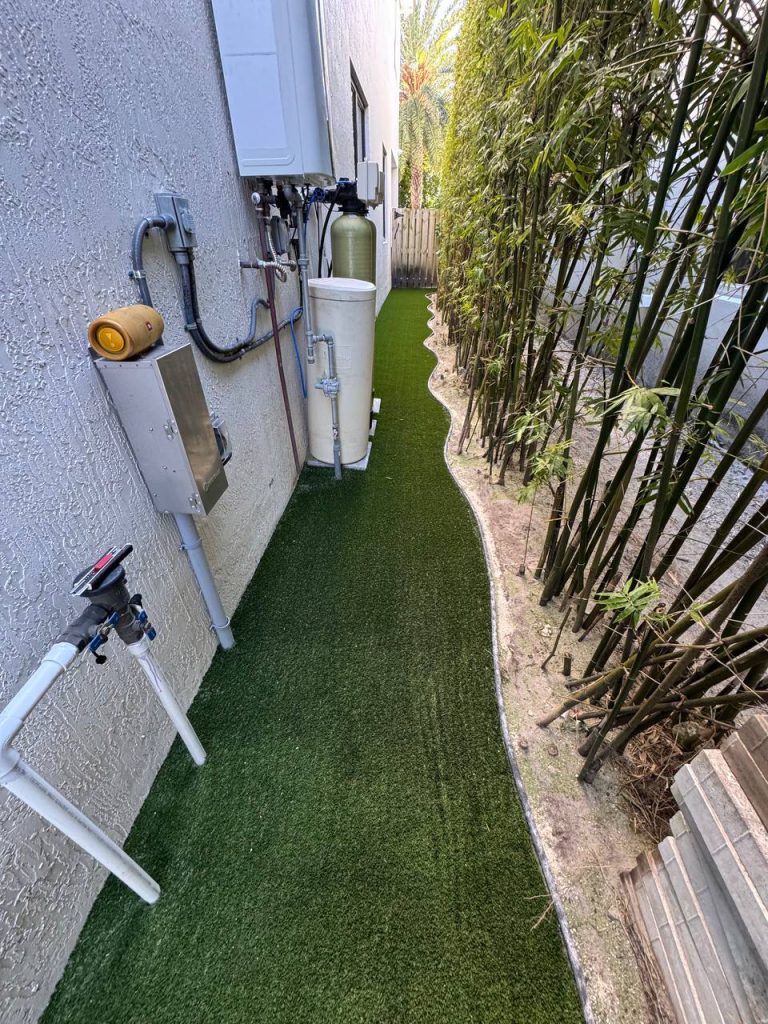 Turf in a narrow passage between a white wall and bamboo.