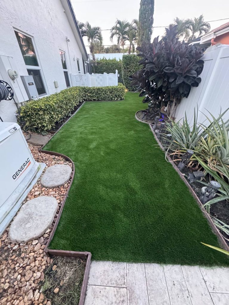 Curving turf lawn bordered by planting, stones and a patio threshold.