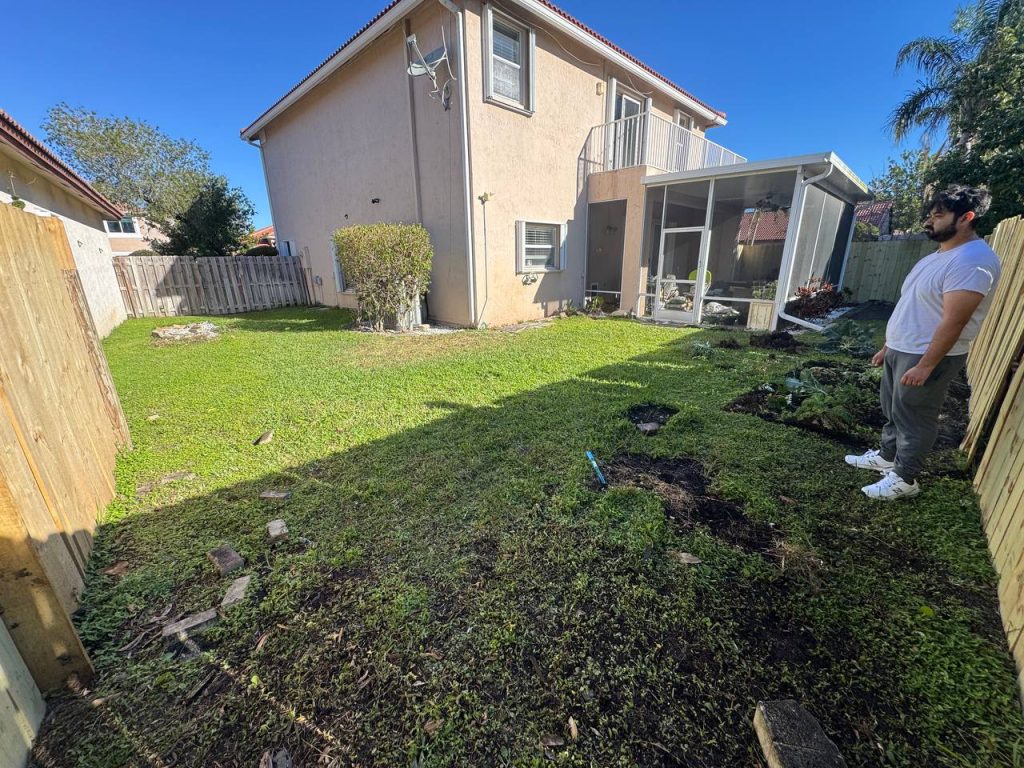 Earlier ground surface beside a two-storey beige house and screened patio.