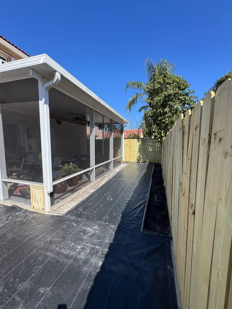 Dark installation underlay beside a two-storey beige house and screened patio.