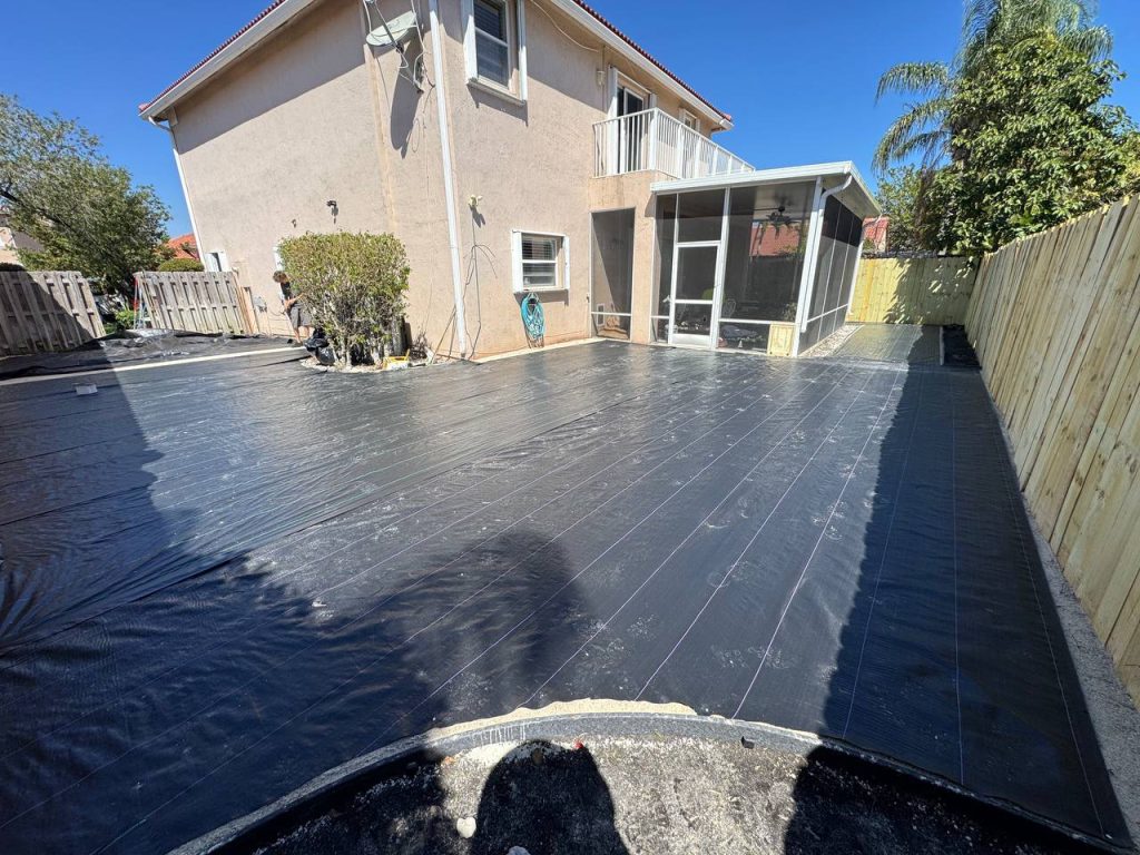 Dark installation underlay beside a two-storey beige house and screened patio.