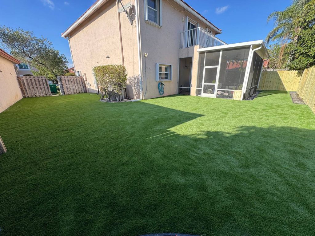 Artificial turf lawn beside a two-storey beige house and screened patio.