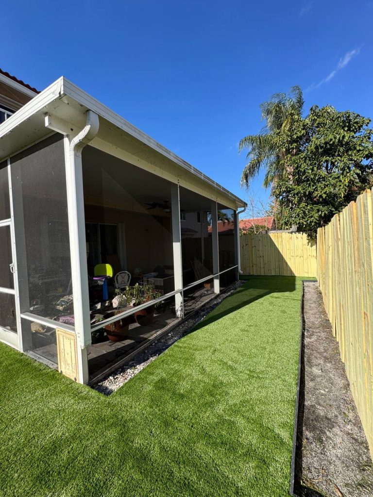 Turf beside a two-storey beige house and screened patio.