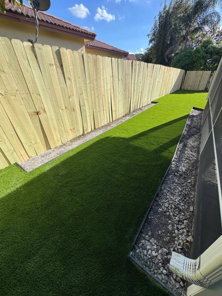 Turf beside a two-storey beige house and screened patio.