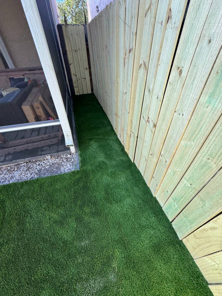 Turf beside a two-storey beige house and screened patio.