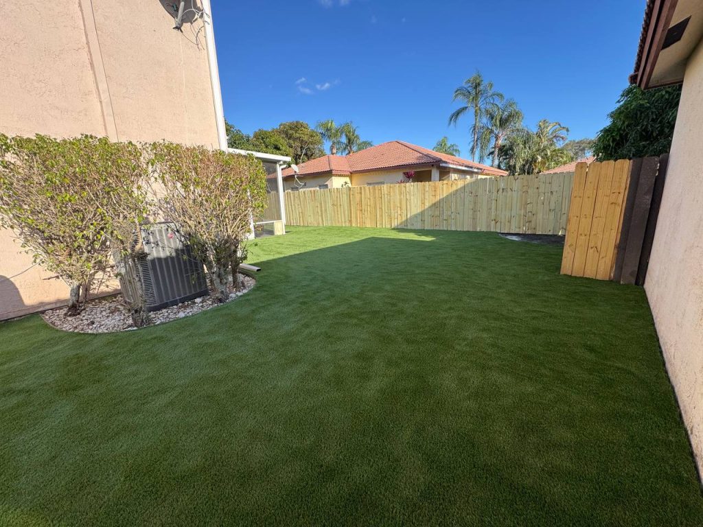 Turf beside a two-storey beige house and screened patio.