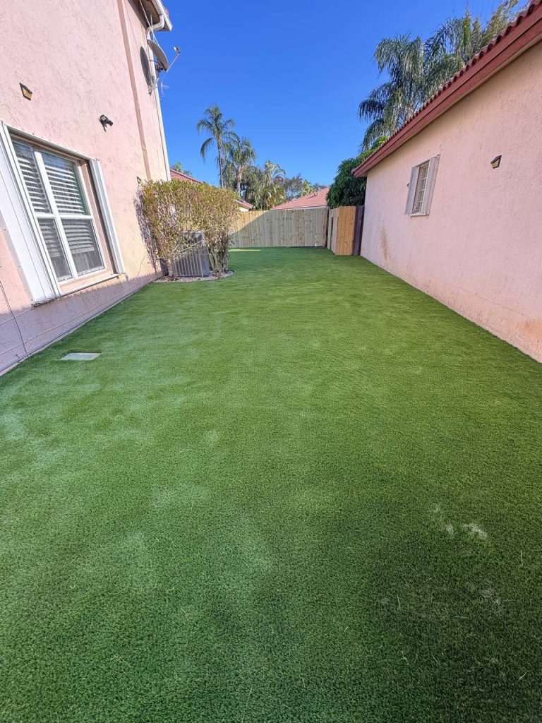 Turf in a side yard bordered by pink walls.