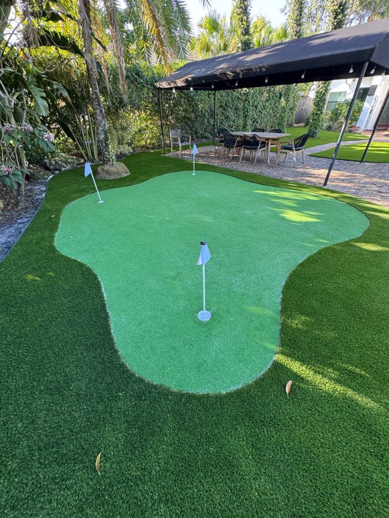 Putting green with flags beside palms and brick paths.