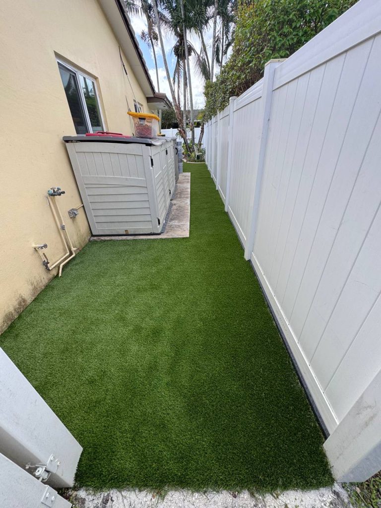 Turf in a curved side garden beside a cream house and white fence.