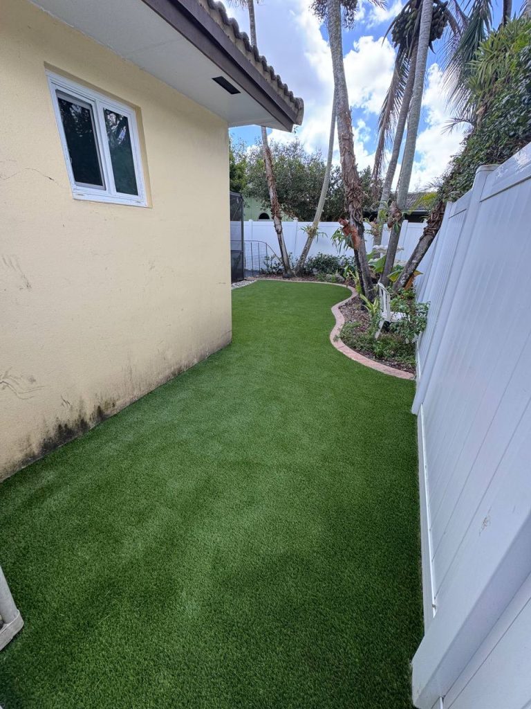 Turf in a curved side garden beside a cream house and white fence.