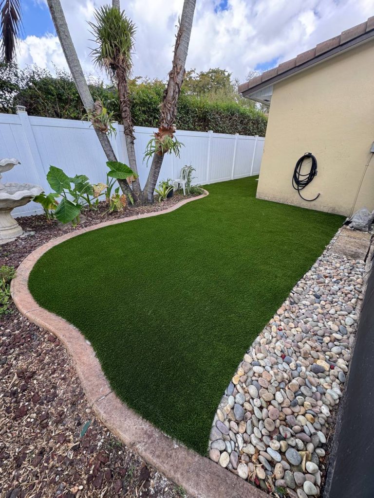 Curved side-garden turf beside a cream wall, palms and a white fence.