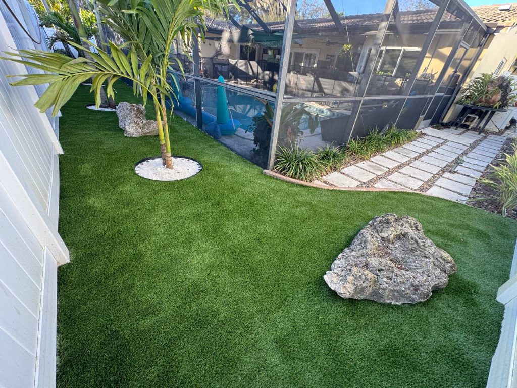 Turf in a curved side garden beside a cream house and white fence.