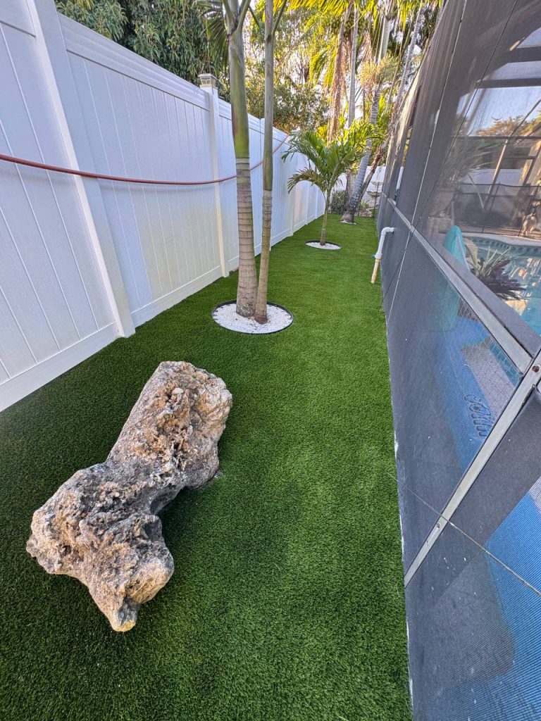 Turf in a curved side garden beside a cream house and white fence.
