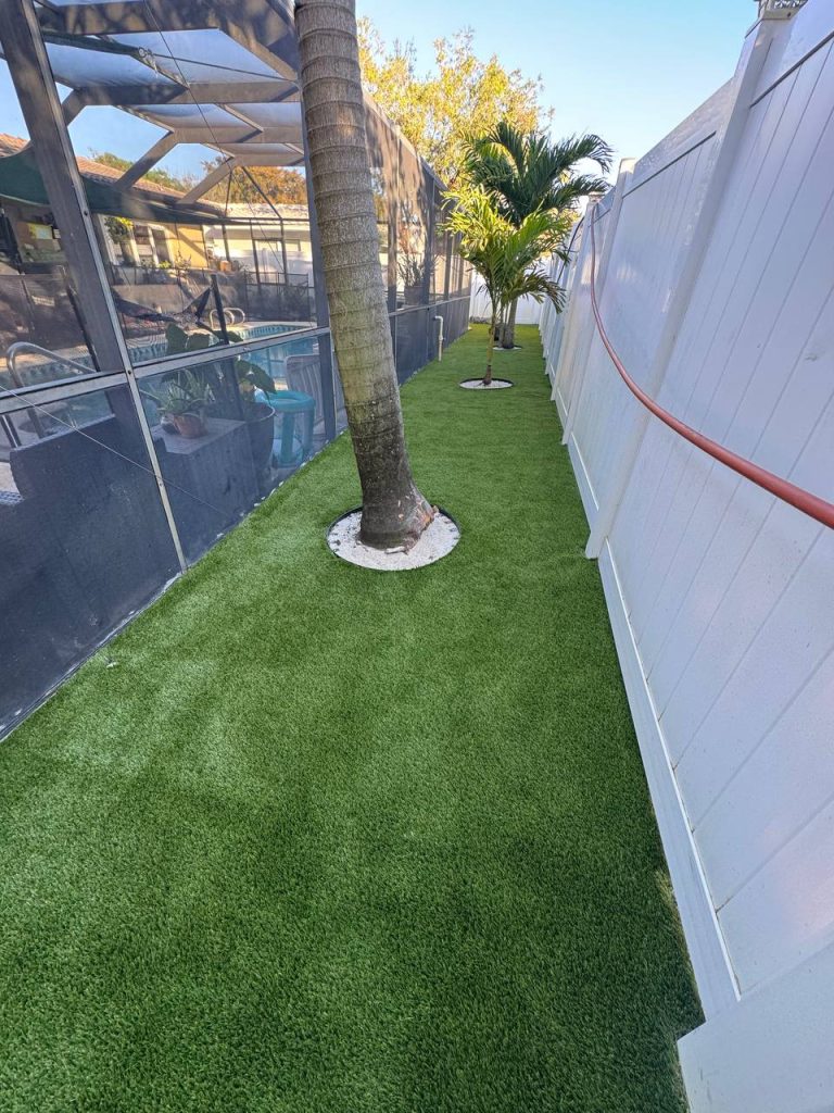 Turf in a curved side garden beside a cream house and white fence.