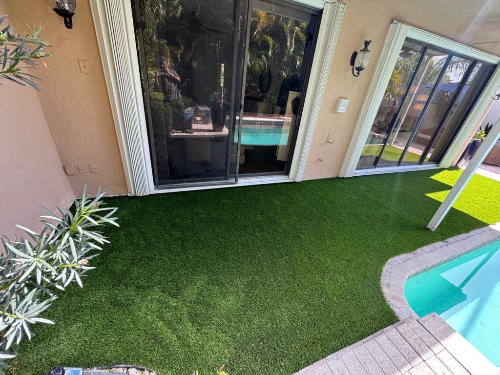 Turf strip beside sliding doors and a swimming pool under a covered patio.