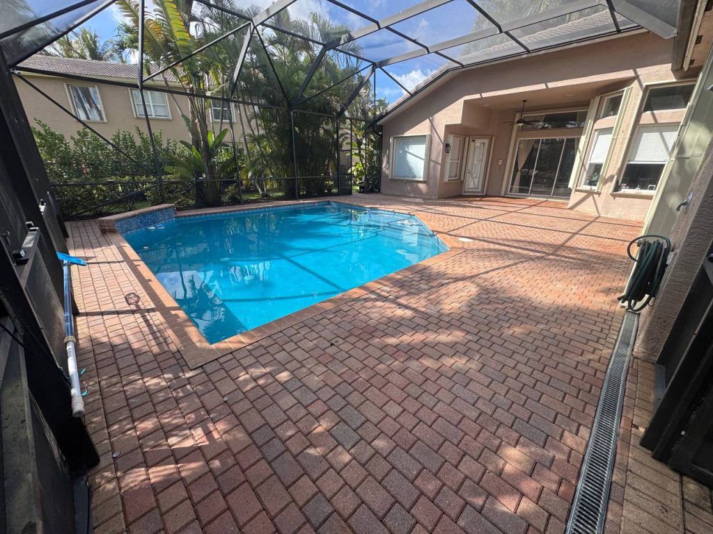 Earlier ground surface around a swimming pool inside a screen enclosure.
