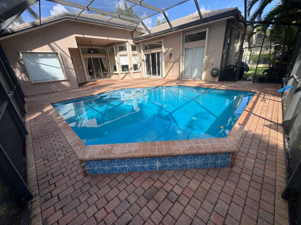 Earlier ground surface around a swimming pool inside a screen enclosure.