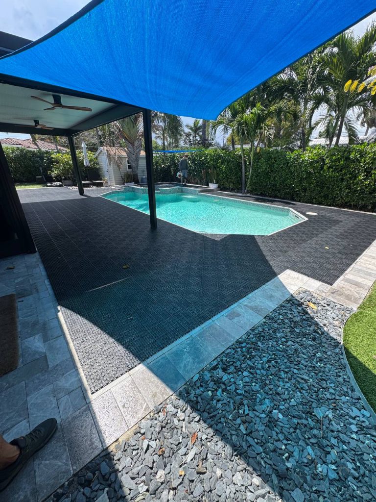 Dark installation underlay around a swimming pool beneath a blue shade sail.