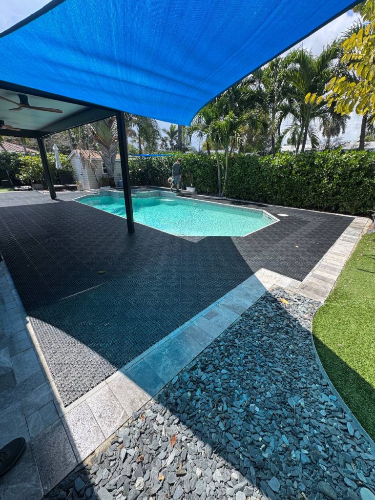 Dark installation underlay around a swimming pool beneath a blue shade sail.
