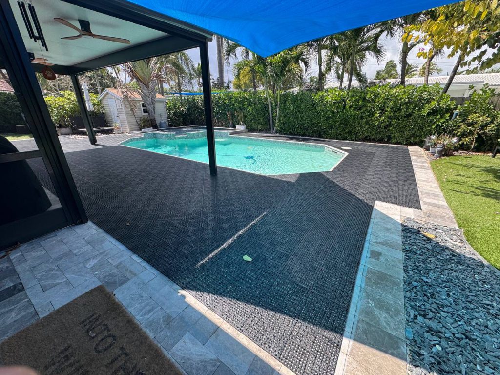 Dark installation underlay around a swimming pool beneath a blue shade sail.