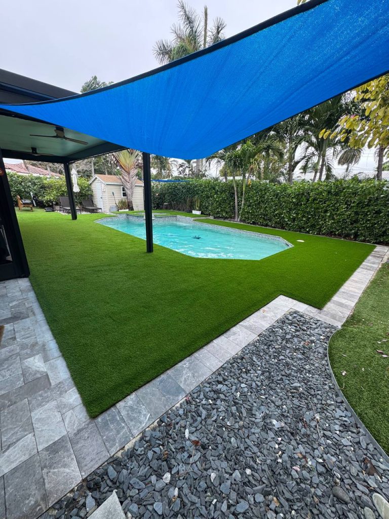 Turf around a swimming pool beneath a blue shade sail.