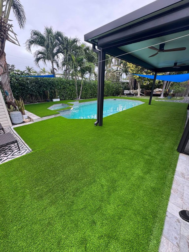 Turf around a swimming pool beneath a blue shade sail.