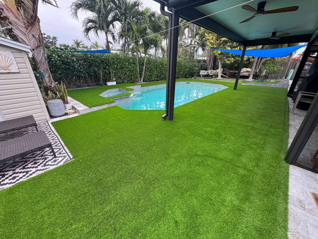 Turf around a swimming pool beneath a blue shade sail.