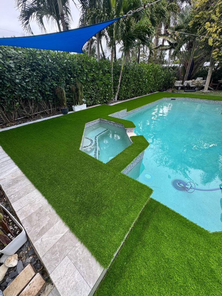 Turf around a swimming pool beneath a blue shade sail.