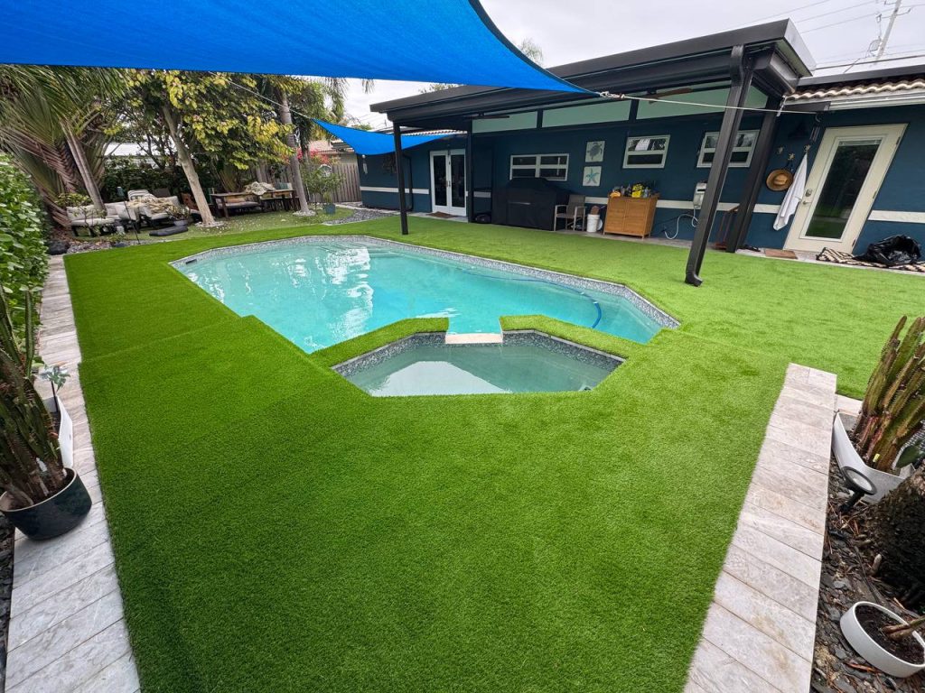 Turf around a swimming pool beneath a blue shade sail.