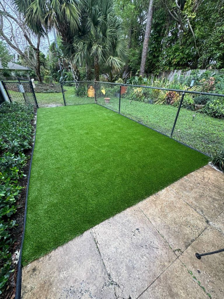 Rectangular turf area beside a concrete patio and chain-link fence.